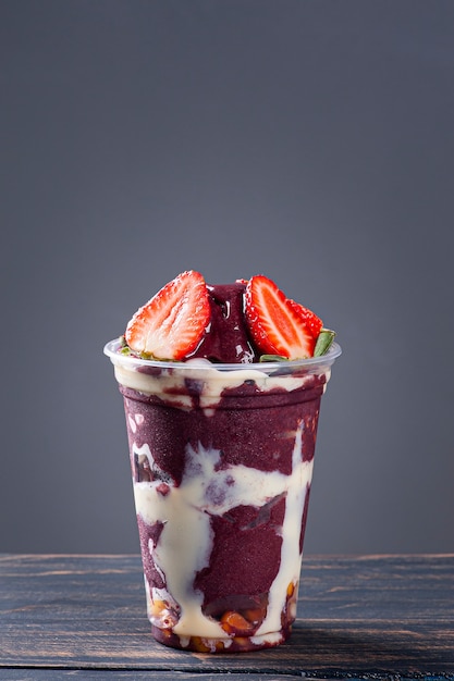 Photo brazilian frozen yoghurt­ in a plastic cup with condensed milk and strawberry. fruit from the amazon. copy space