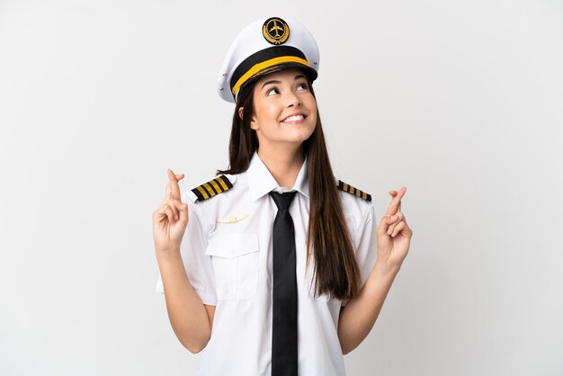 Brazilian girl Airplane pilot over isolated white background with fingers crossing