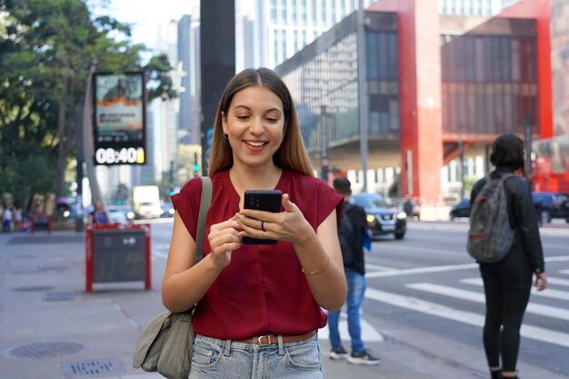 Photo brazilian girl using mobile phone with blurred background on paulista avenue in sao paulo brazil