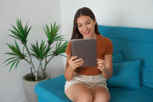 家のソファに座ってタブレットPCを使っているブラジルの女の子