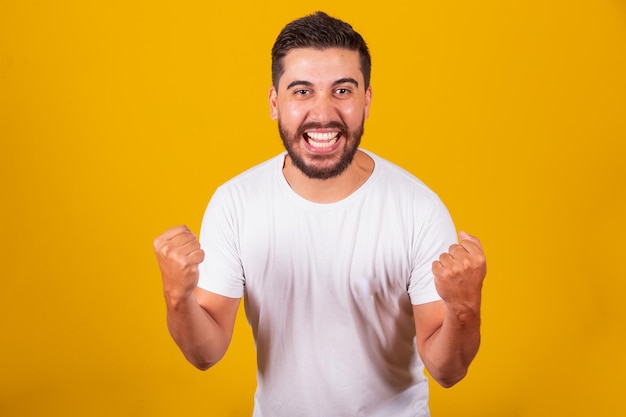 Brazilian Latin American man with arms celebrating Screaming with happiness like a winner joyful happy confident yellow background