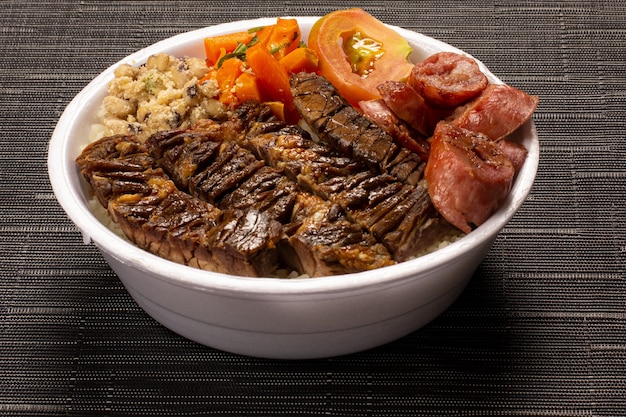 Brazilian lunchbox with barbecue meat sausage salad rice beans and farofa