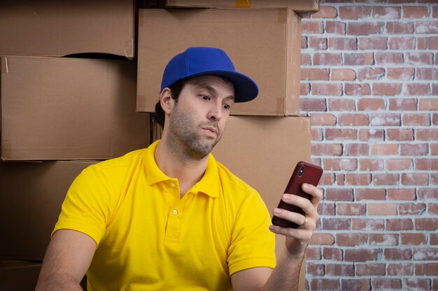 Brazilian mailman using a smartphone in front of a lot of packages in a deposit