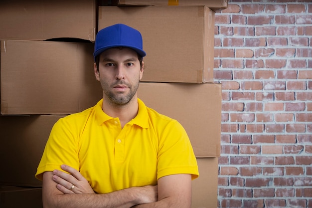 Brazilian mailman with arms crossed in a deposit with a a lot of boxes.