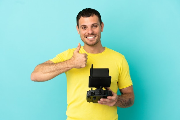 Brazilian man holding a drone remote control over isolated blue background giving a thumbs up gesture