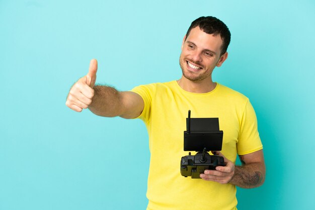 Бразильский мужчина держит пульт дистанционного управления дроном на изолированном синем фоне, показывая жест рукой