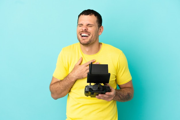 Brazilian man holding a drone remote control over isolated blue background smiling a lot