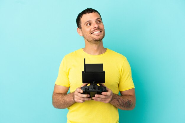Brazilian man holding a drone remote control over isolated blue background thinking an idea while looking up