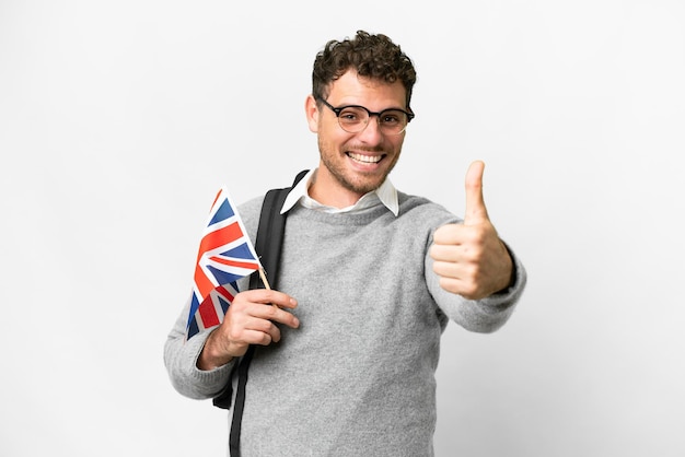 Brazilian man holding an United Kingdom flag over isolated white background with thumbs up because something good has happened