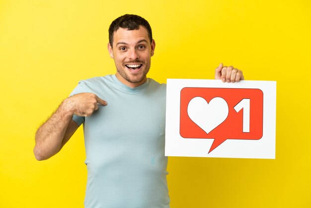 Brazilian man over isolated purple background holding a placard with Like icon and pointing it