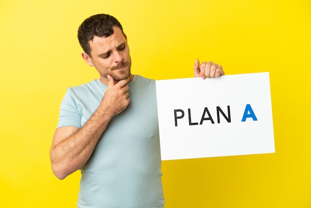 Brazilian man over isolated purple background holding a placard with the message PLAN A and thinking