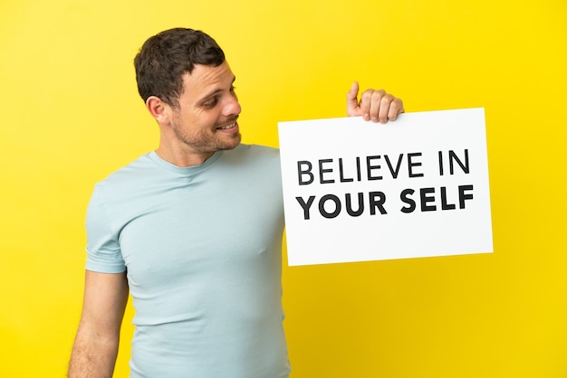 Photo brazilian man over isolated purple background holding a placard with text believe in your self