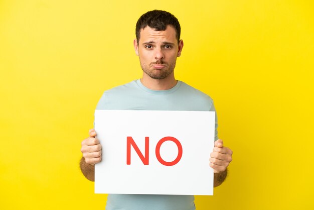 Photo brazilian man over isolated purple background holding a placard with text no with sad expression