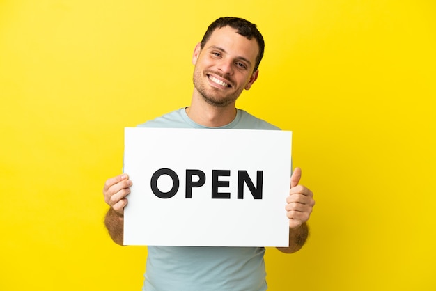 Brazilian man over isolated purple background holding a placard with text OPEN with happy expression