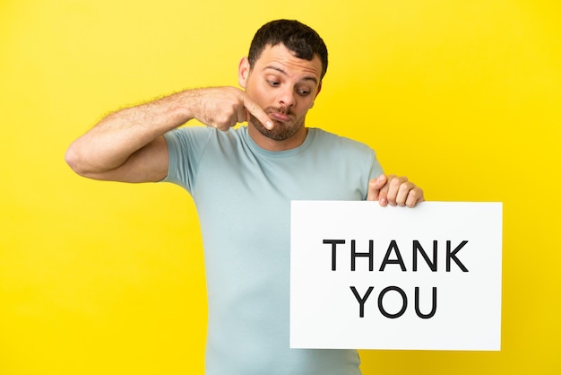 Brazilian man over isolated purple background holding a placard with text THANK YOU and  pointing it