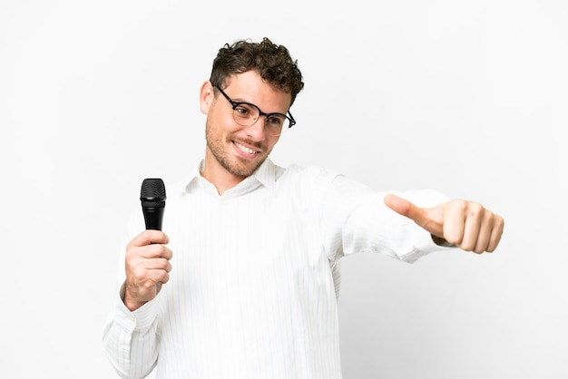 Brazilian man picking up a microphone over isolated white background giving a thumbs up gesture