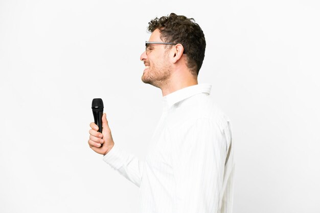 Photo brazilian man picking up a microphone over isolated white background laughing in lateral position