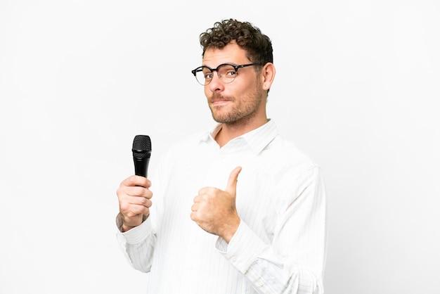 Photo brazilian man picking up a microphone over isolated white background proud and selfsatisfied