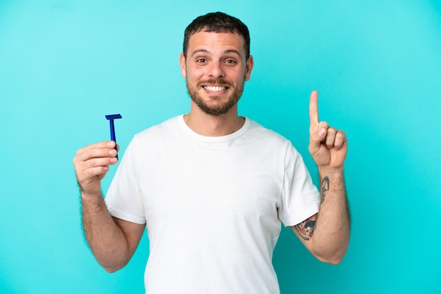 Brazilian man shaving his beard isolated on blue background pointing up a great idea