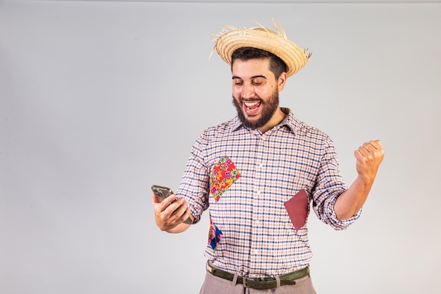 Brazilian man wearing festa junina clothes Arraial Feast of Saint John with smartphone browsing mobile apps