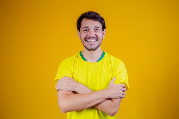 黄色の背景に腕を組んでブラジルのTシャツとブラジル人男性