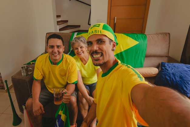 Foto famiglia brasiliana di razza mista celebrando la coppa in soggiorno guardando la partita di calcio famiglia che scatta foto selfie mentre guarda la partita di coppa