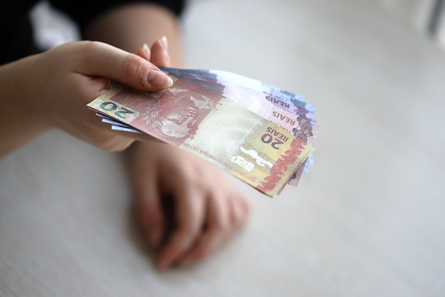 Photo brazilian money bills in woman hand female gives bunch of brazilian reais to us