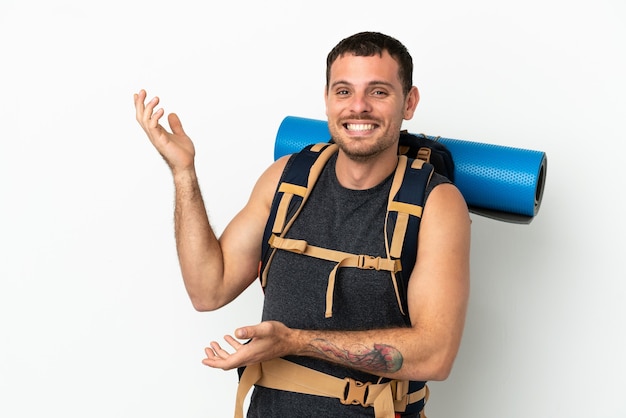 Brazilian mountaineer man with a big backpack over isolated white background extending hands to the side for inviting to come