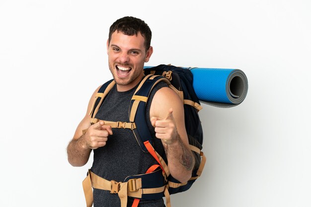 Brazilian mountaineer man with a big backpack over isolated white background pointing to the front and smiling