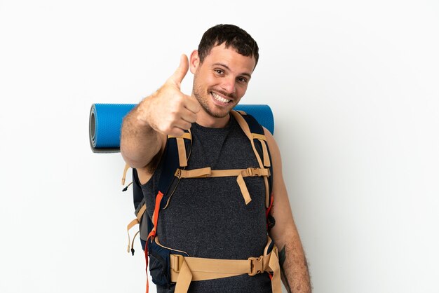 Brazilian mountaineer man with a big backpack over isolated white background with thumbs up because something good has happened