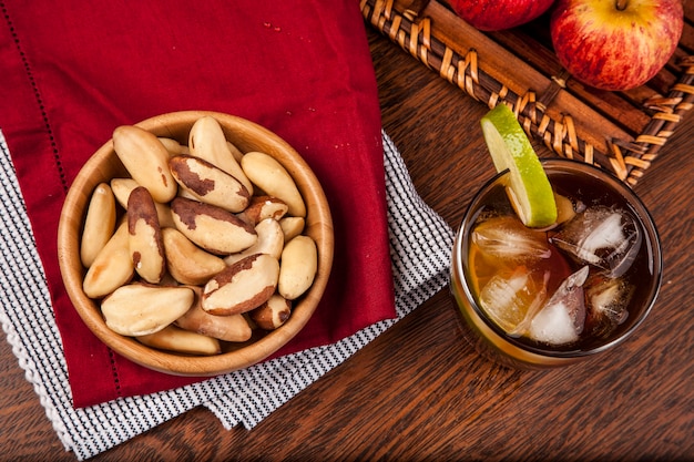 Brazilian nuts on a wooden table with apples and ice tea in the background.