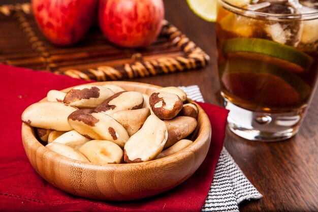 Brazilian nuts on a wooden table with apples and ice tea in the background.