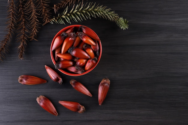 Brazilian pinion nuts in brown and red wooden bowl on gray wooden background.