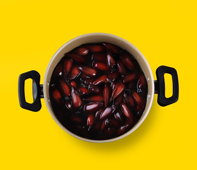 Brazilian pinion nuts in brown and red wooden bowl on yellow background.