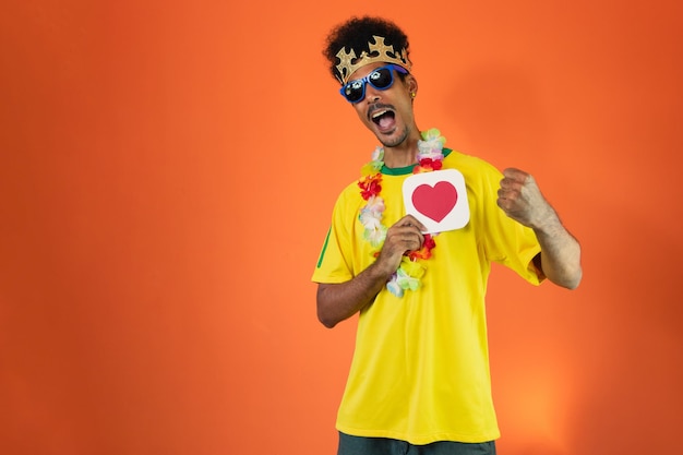 オレンジ色の背景に分離された黄色の T シャツで祝うブラジル人プレーヤー黒人男性