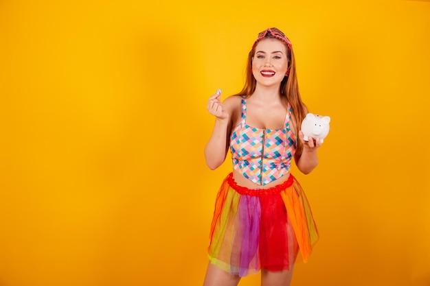 Brazilian redhead in carnival clothes holding piggy bank and coin