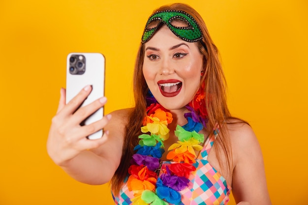 Brazilian redhead in carnival clothes with a necklace of flowers around her neck showing smartphone