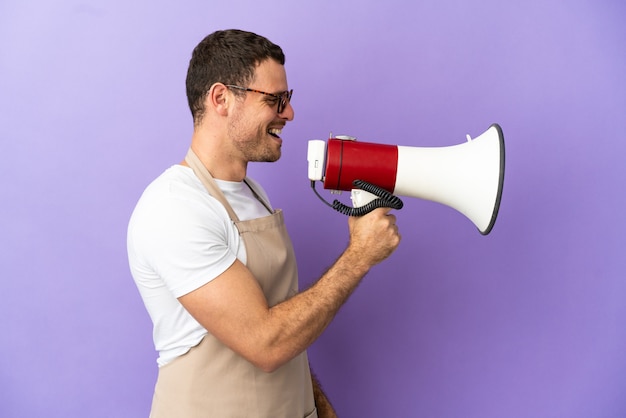 Brazilian restaurant waiter over isolated purple background shouting through a megaphone