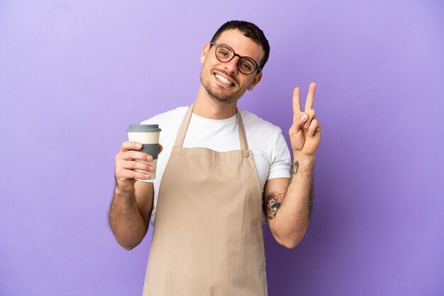 両手で勝利のサインを示す孤立した紫色の背景の上のブラジル料理レストランウェイター