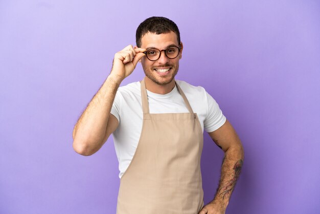 Photo brazilian restaurant waiter over isolated purple background with glasses and happy