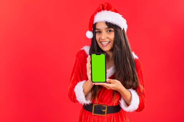 Foto adolescente brasiliana che indossa abiti di natale mostra uno smartphone con schermo verde nell'app pubblicitaria mobile chroma key