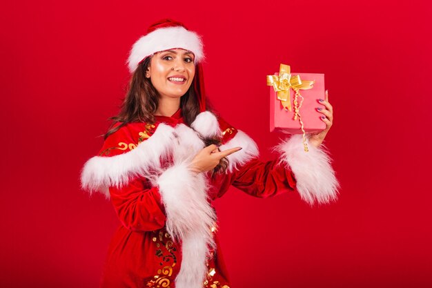 Brazilian woman dressed in christmas clothes santa claus showing a red gift