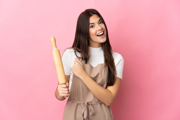 Brazilian woman holding a rolling pin isolated on pink celebrating a victory