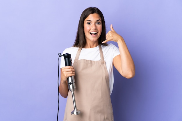 Brazilian woman using hand blender isolated on purple wall making phone gesture. Call me back sign