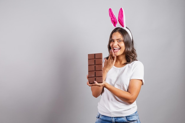 Brazilian woman with Easter bunny ears smiling happily holding Easter chocolate bar