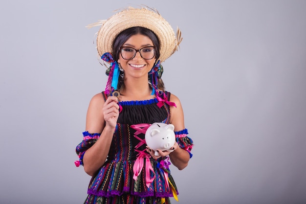 Brazilian woman with festa junina clothes holding piggy bank and coin