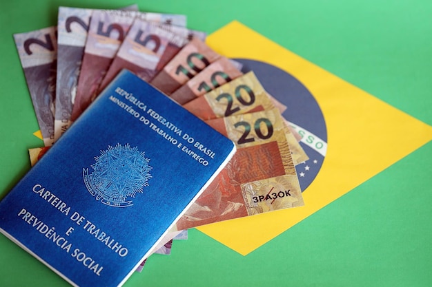 Brazilian work card and social security blue book and reais money bills on flag of federative