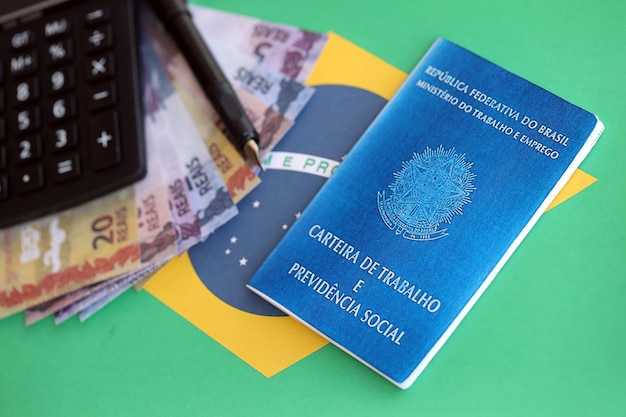 Photo brazilian work card and social security blue book and reais money bills with calculator and pen on