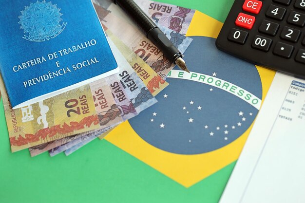 Brazilian work card and social security blue book and reais money bills with calculator and pen on