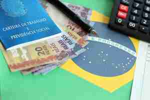 Photo brazilian work card and social security blue book and reais money bills with calculator and pen on